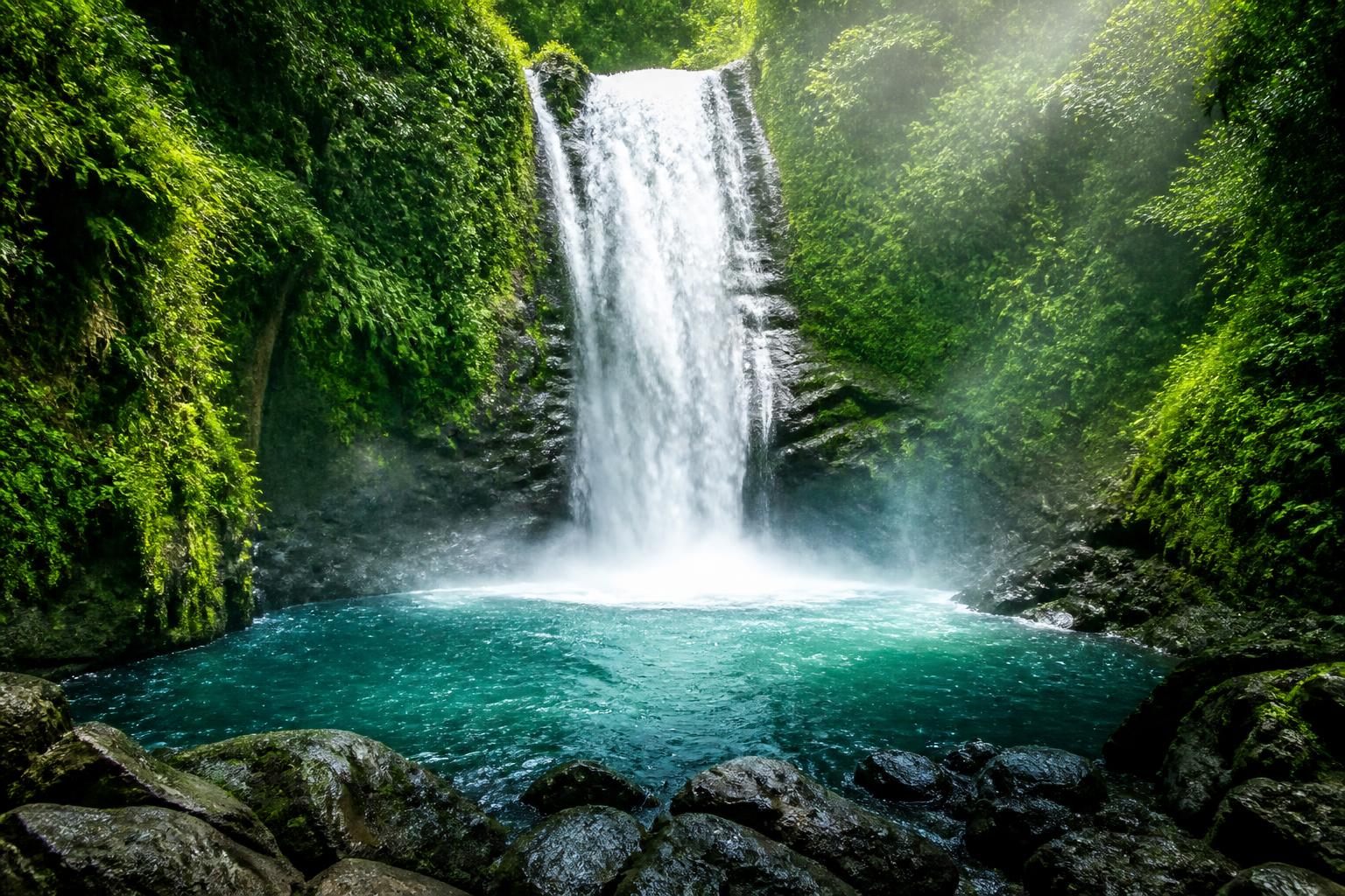 Cachoeira majestosa cercada por floresta tropical densa com água caindo em uma piscina cristalina abaixo.