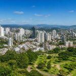 Vista panorâmica de cidades próximas a Belo Horizonte com prédios, áreas verdes e céu azul.