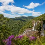 Paisagem natural com colinas verdes, vegetação densa, rio ou cachoeira e céu azul perto de Curitiba.